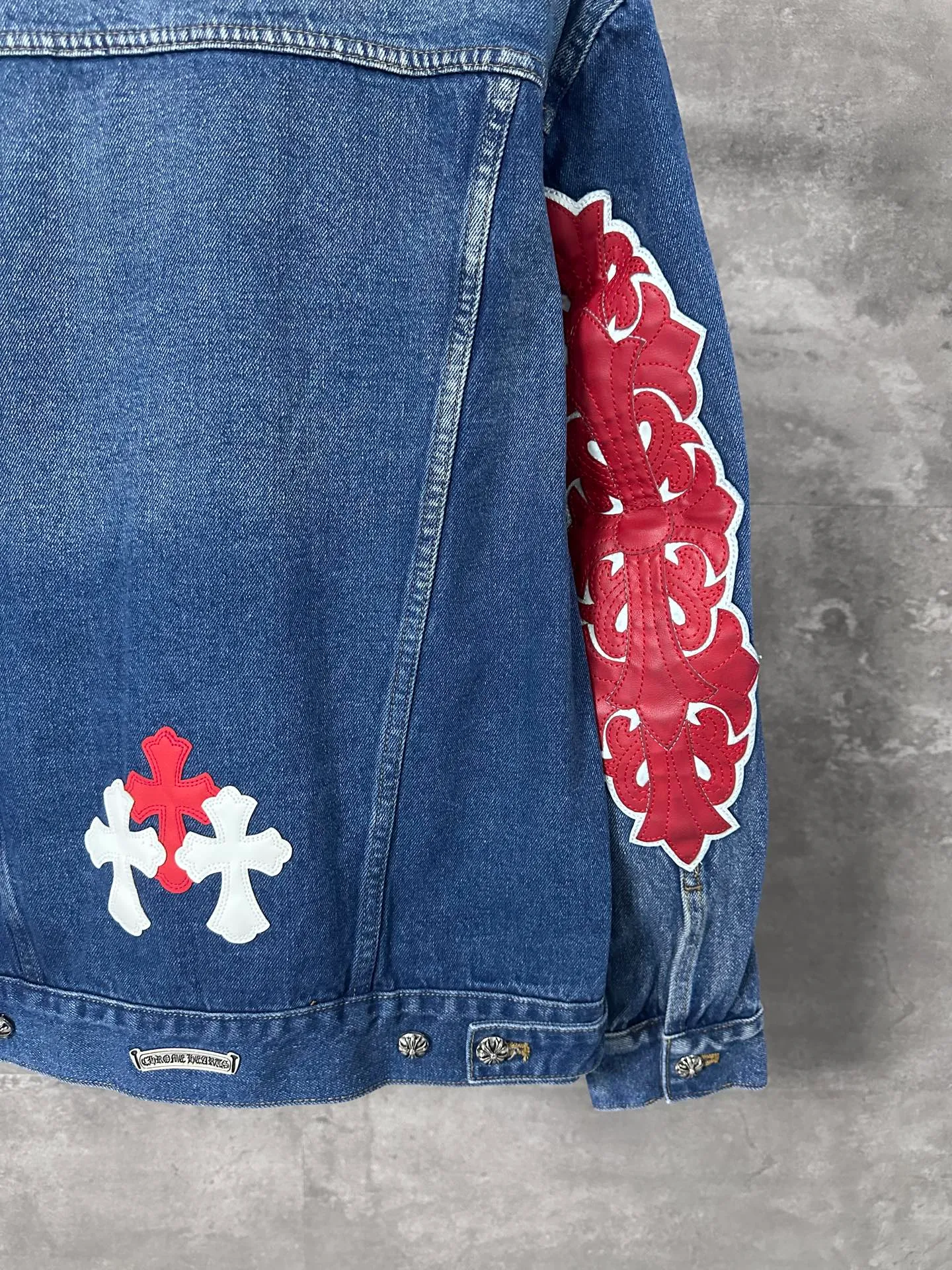 P720 CHrome Hearte cross patchwork leather denim jacket size: S M L Design details: the visual fantasy of Gothic symbols, the multi-dimensional expression of the cross totem: the red and white contrasting cross patches are staggered on the chest and back, making the brand more recognizable; the hollow cross pattern leather splicing on the sleeves combines the mystery of religious symbols with the punk-style deconstructed design. Every detail tells the dark aesthetics of Crowe's heart. Retro distressing with denim texture: Selected denim fabrics are treated with distressing techniques to show natural fading and texture, which not only retains the retro accent of denim items, but also adds a casual sense to the overall look. The ingenuity of hardware and tailoring: The metal buttons and hardware all have Croxin's iconic pattern, which shines exquisitely under the refraction of light; the neat tailoring of the classic denim jacket is suitable for a variety of wearing scenarios, and can create a strong personal style whether it is layered or worn alone. Croxin's denim jacket is not only a piece of clothing, but also a style badge that highlights unique aesthetics and rebellious attitude. For those who pursue individuality, they can leave their own hardcore mark in the fashion field.